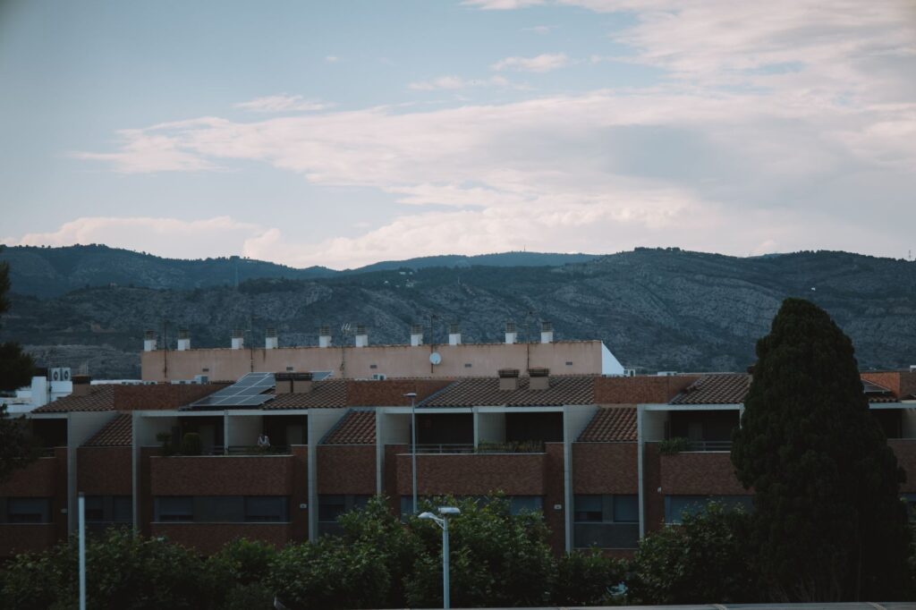 Modern residential buildings in Valencia, Spain, set against a scenic mountain range under a cloudy
