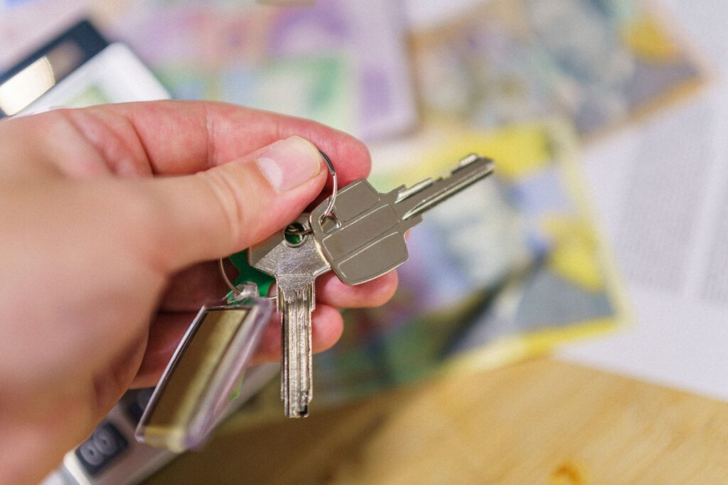 Close-up of keys in hand representing property ownership with blurred financial documents in the bac